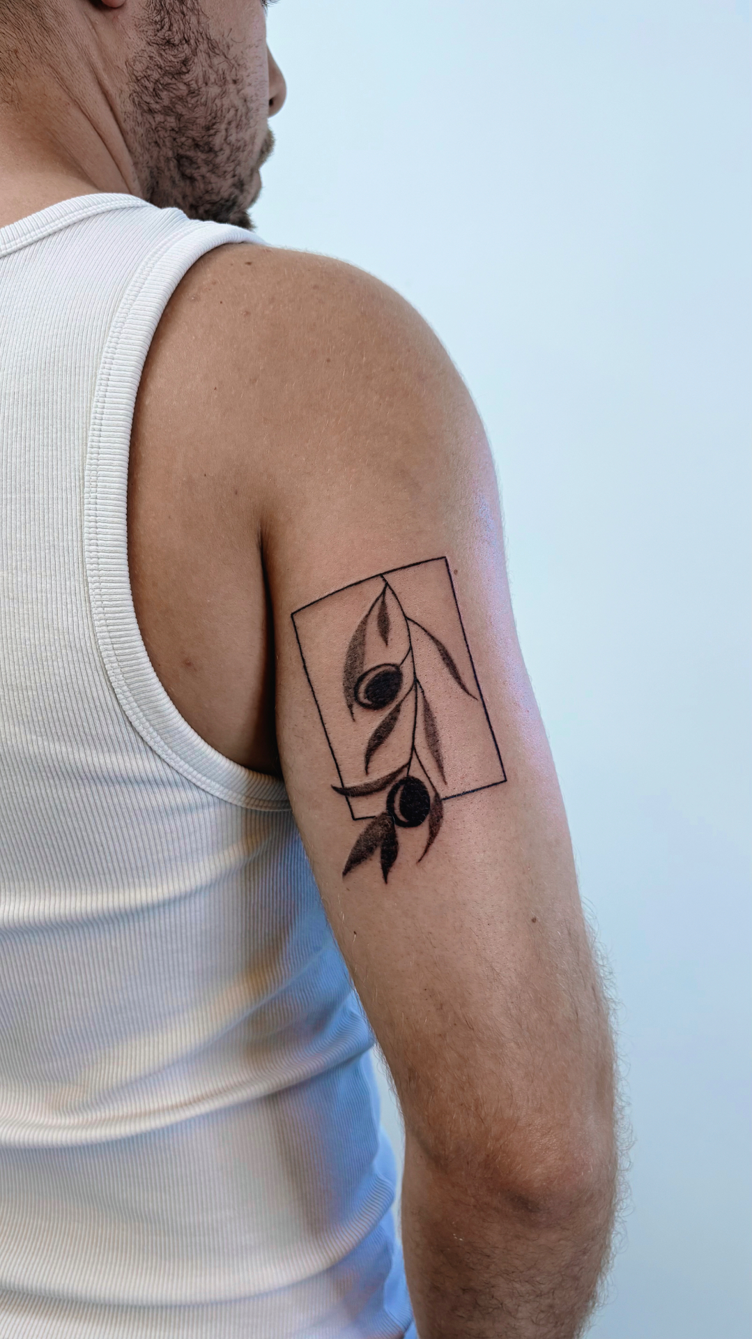 Olive branch with two olives breaking out of a rectangular frame on an upper arm