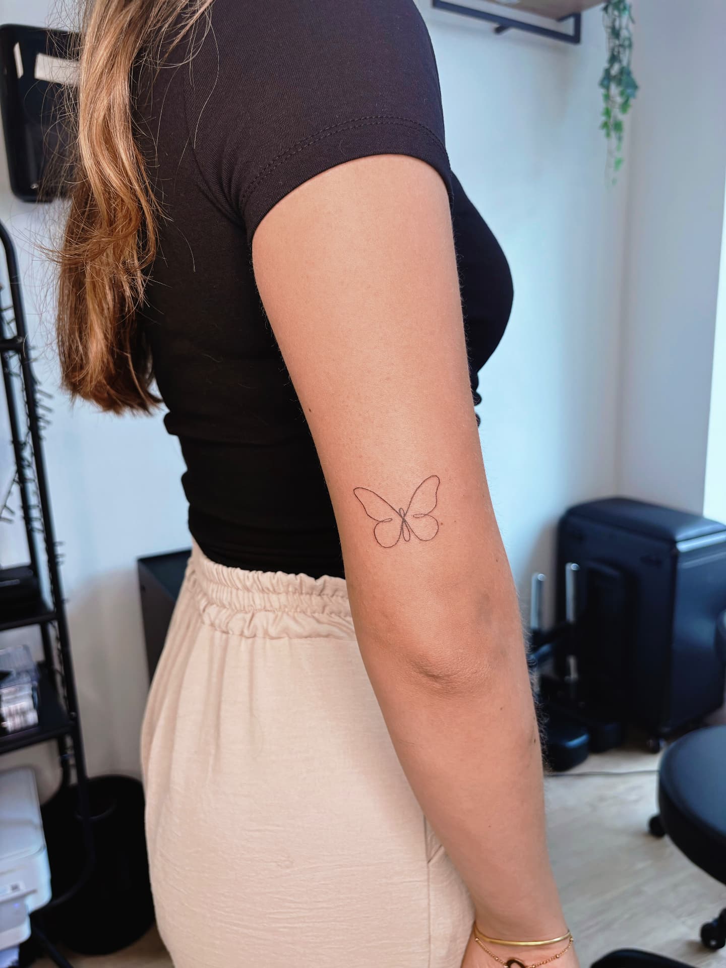 Minimalist fine line butterfly tattoo above the elbow