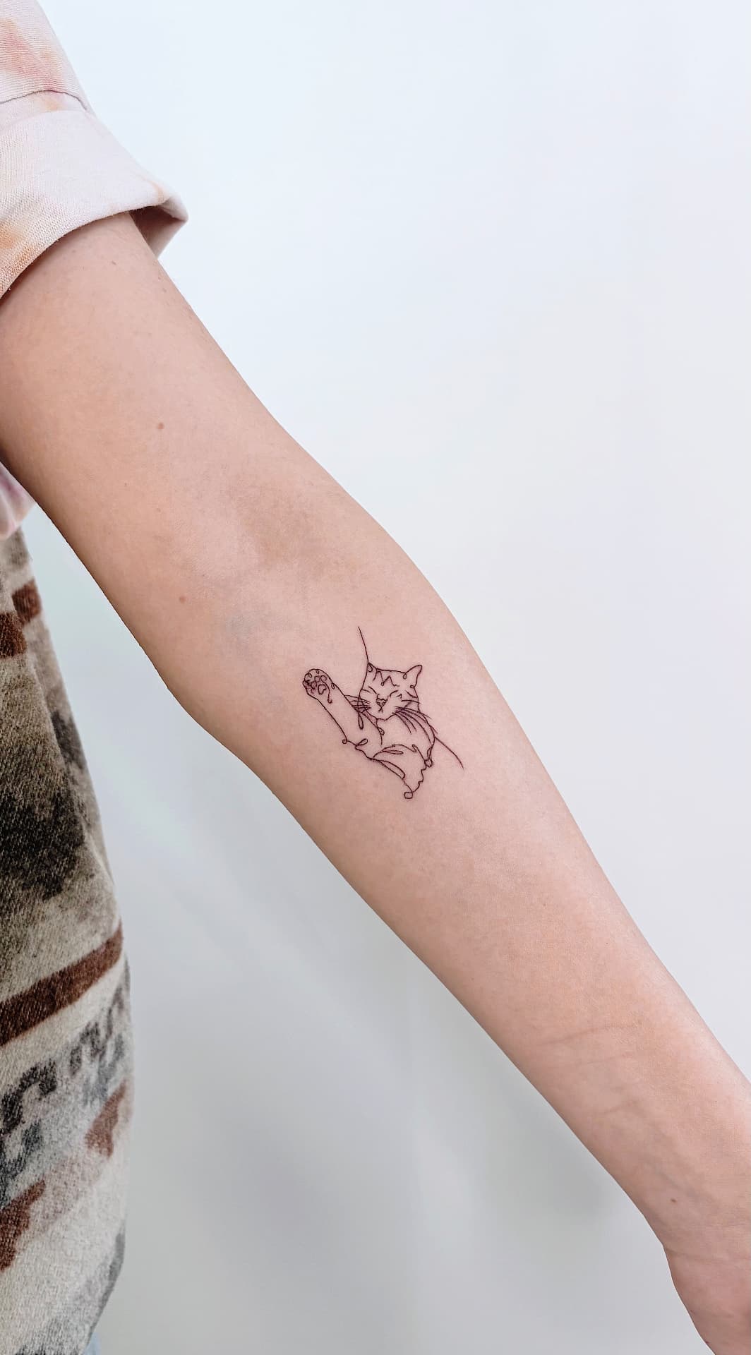 Fine line cat stretching tattooed on the inner forearm