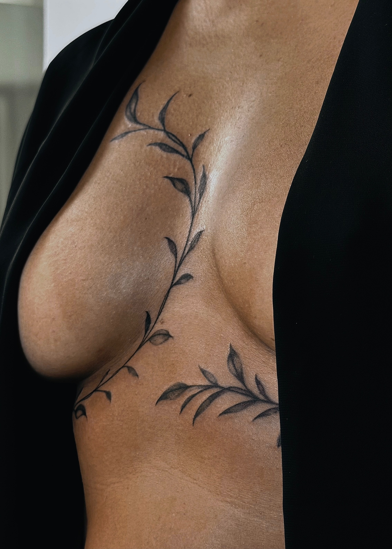 Botanical leafy vine tattoo curving across the sternum and ribs